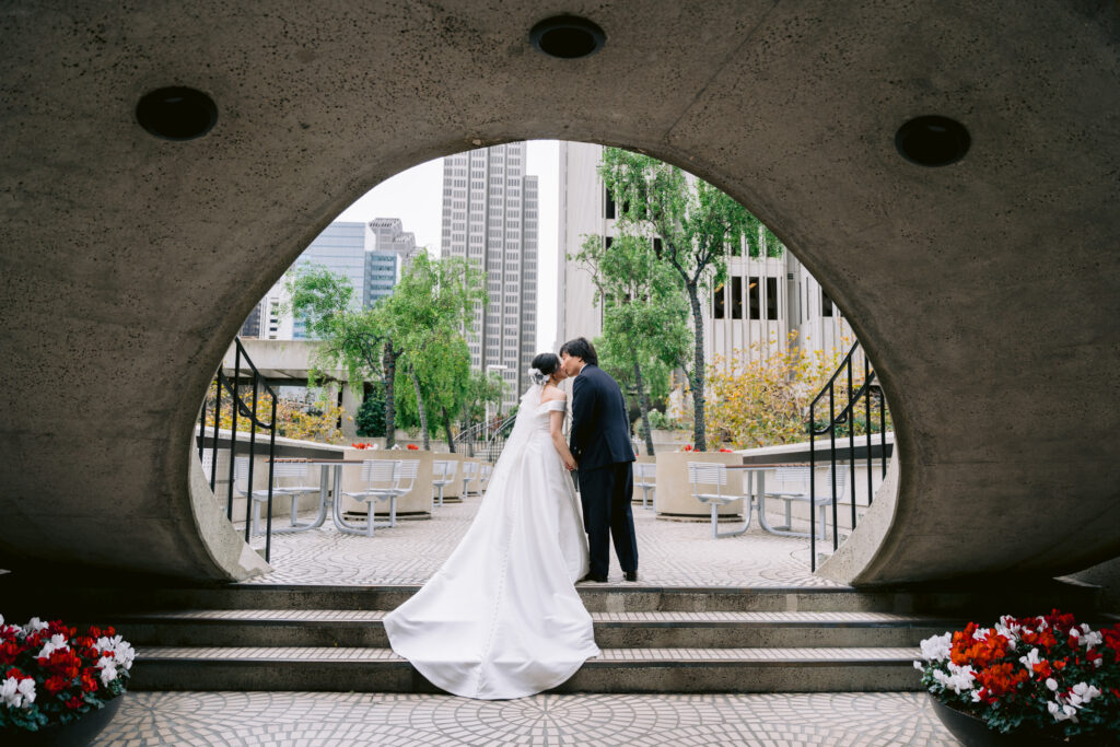 Bride and groom sharing a kiss under an architectural archway in downtown San Francisco during their wedding portrait session.