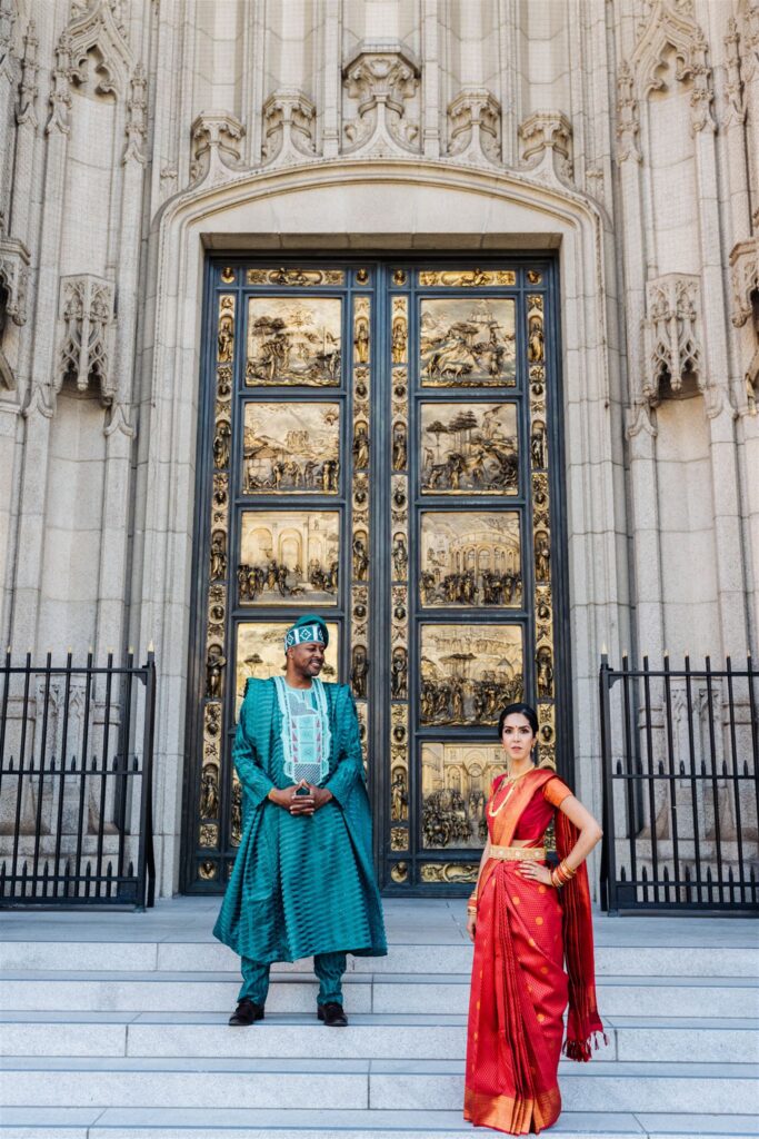 Couple in traditional African and South Asian wedding attire standing on the steps of a grand cathedral with ornate gold doors in San Francisco.