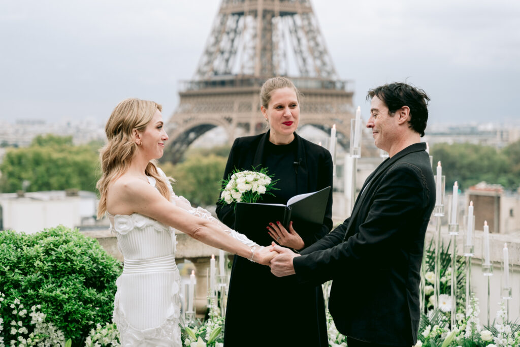 Bride and groom holding hands during their wedding ceremony with the Eiffel Tower in the backgrond. Captured by Fioroni Photography